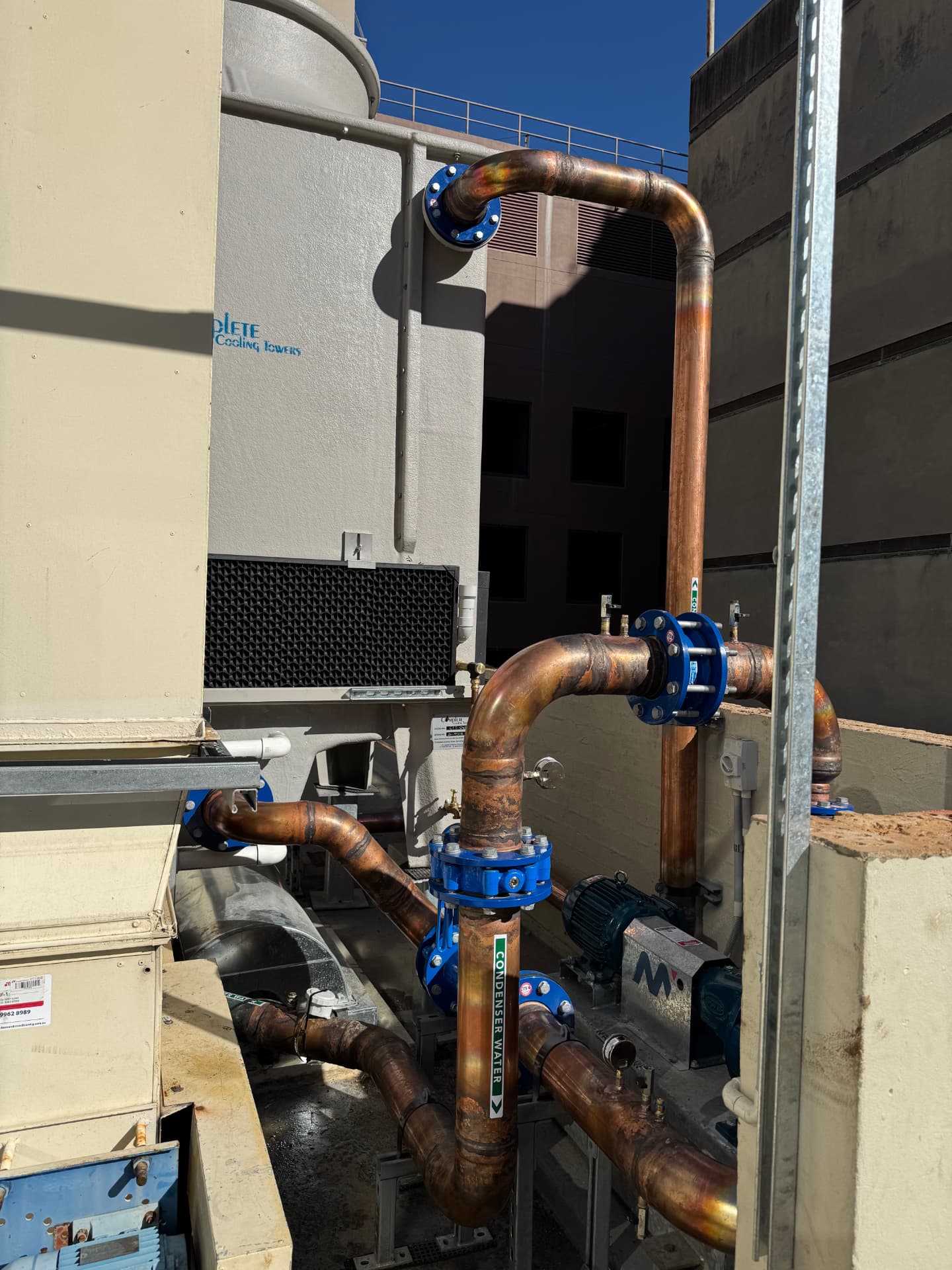 Rooftop cooling tower plant with large copper condenser water mains rising into the towers, flanged valves and strut supports
