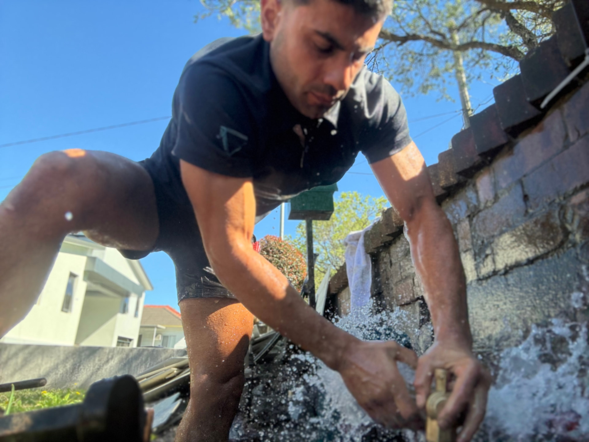 Prevail Plumbing tradesperson isolating and repairing a burst water meter with water spraying