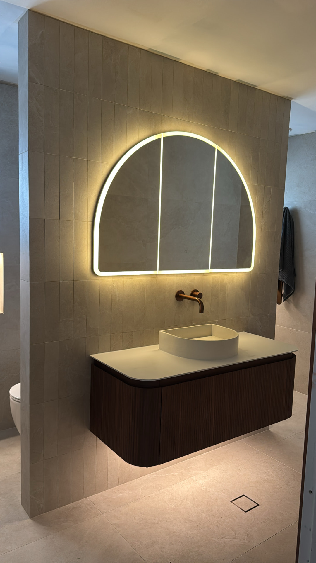 Completed Sydney bathroom fit-off with backlit arch mirror, floating timber vanity and brushed copper wall-mounted tapware