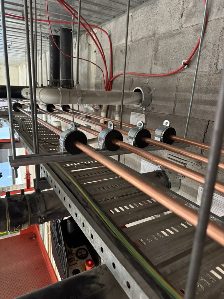 Commercial copper pipework supported on strut above a cable tray in a plant corridor