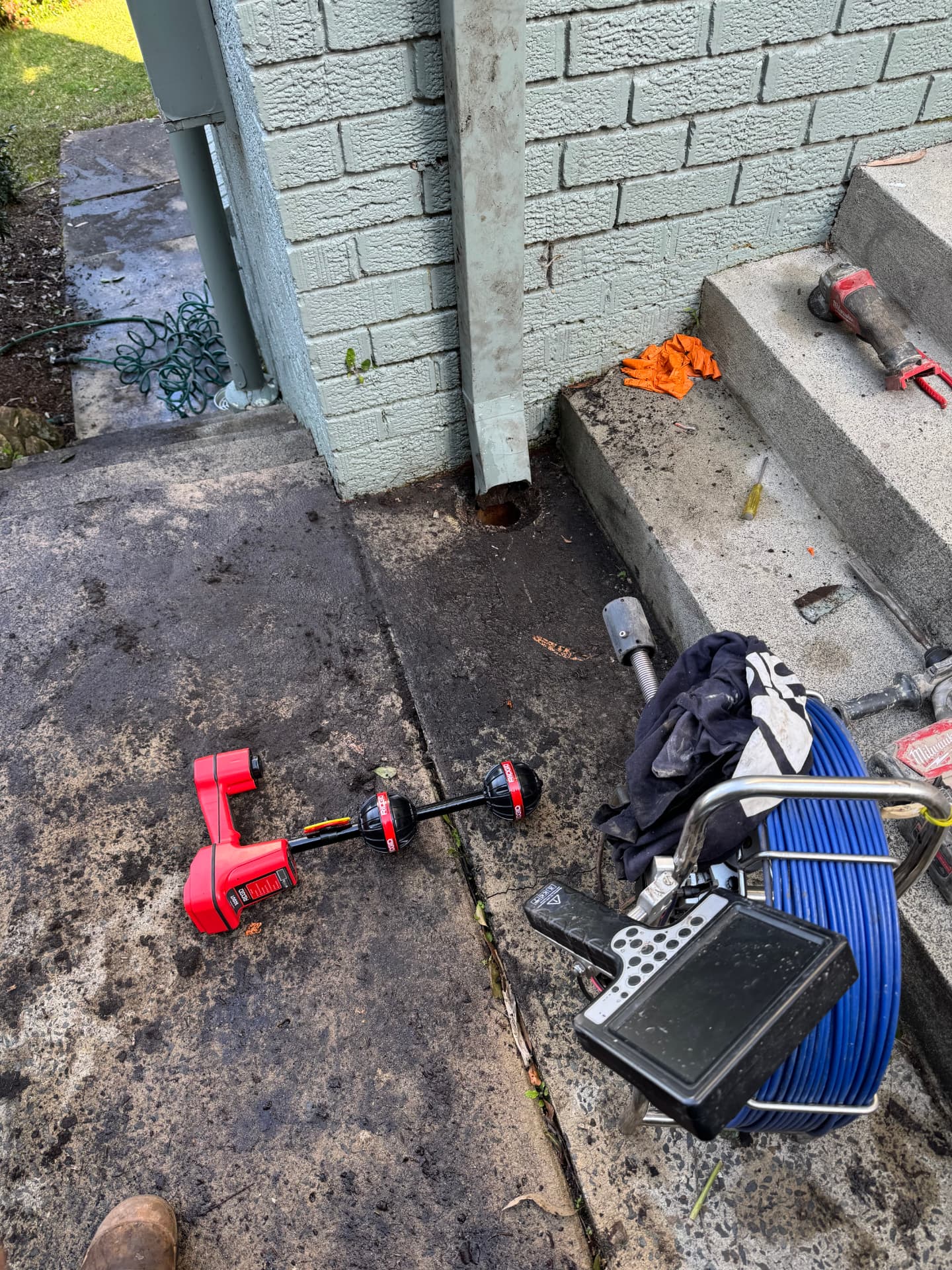 CCTV drain camera reel and pipe locator set up beside a core-drilled drain access point on a residential path