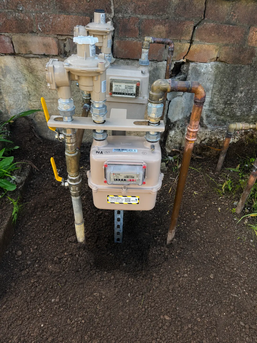 Natural gas meter and regulator assembly with new copper gas service pipework, isolation valves and fittings installed against a brick wall
