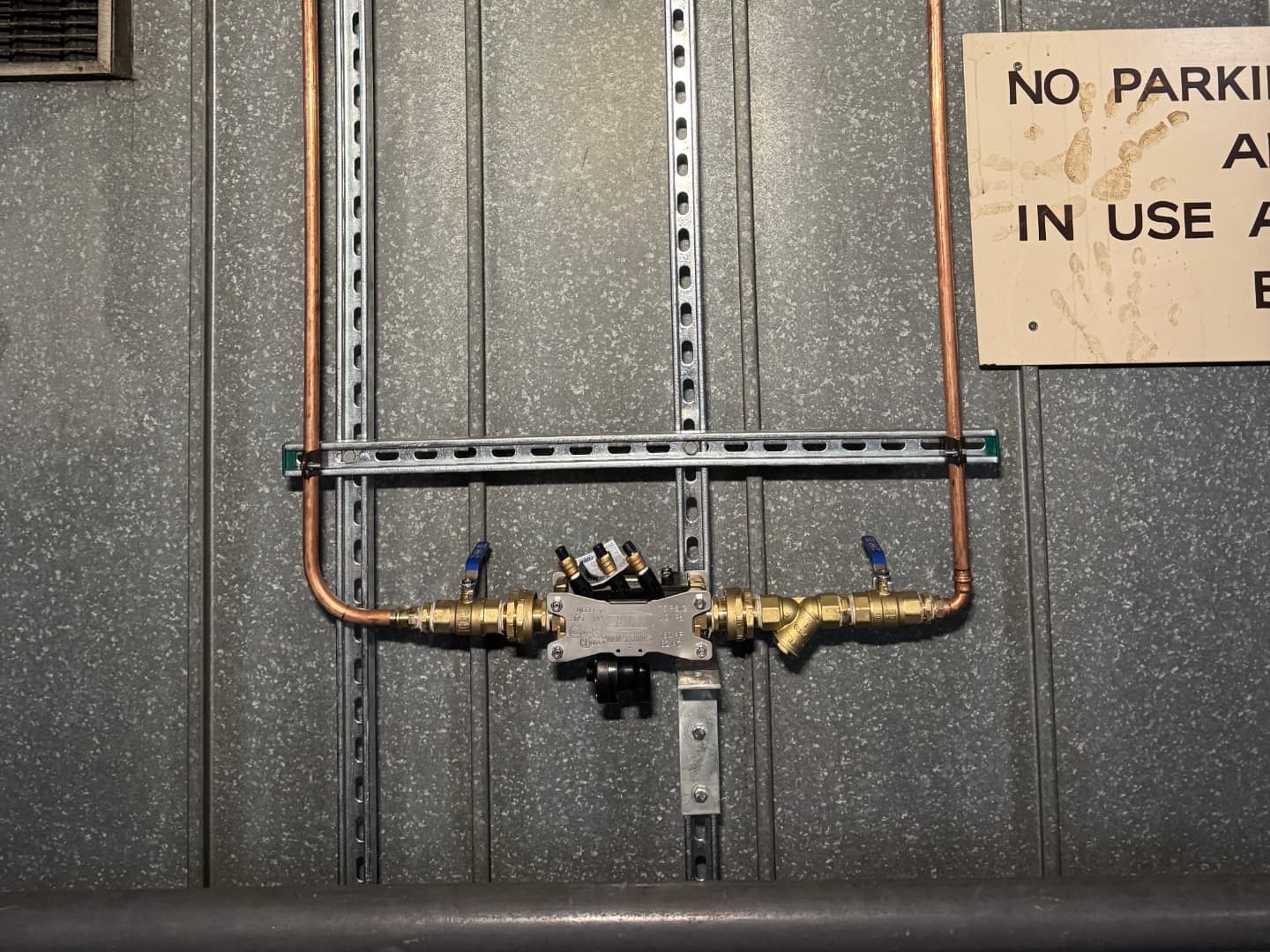 Strut-mounted reduced pressure zone backflow prevention device with brass isolation valves, test cocks and copper pipework installed against a concrete wall